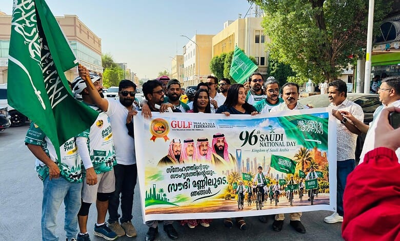 Group of people celebrating Saudi National Day with flags and a banner in the street.