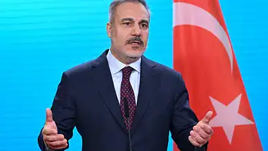 Turkish official speaking at a press conference with the Turkish flag in the background.