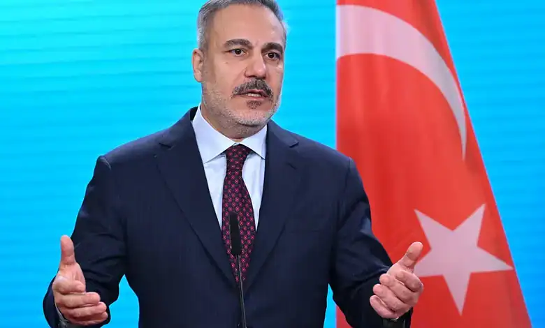 Turkish official speaking at a press conference with the Turkish flag in the background.