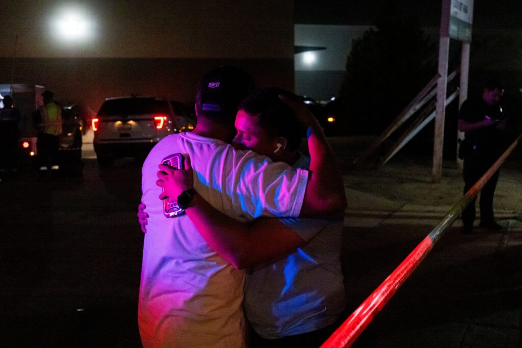Nighttime scene of two people embracing at the scene of a helicopter crash in Los Angeles.
