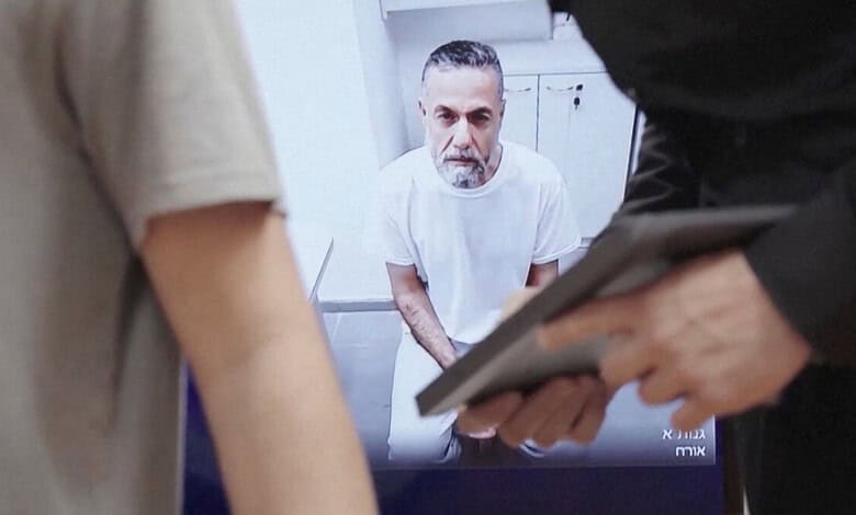 Gaza doctor giving testimony in prison, surrounded by officials, holding a document.