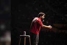 Samay Raina performing stand-up comedy on stage with a microphone in hand.