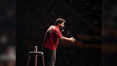Samay Raina performing stand-up comedy on stage with a microphone in hand.