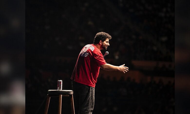 Samay Raina performing stand-up comedy on stage with a microphone in hand.