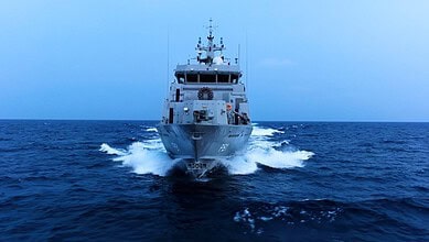 Military ship sailing on the ocean during daytime, with a clear blue sky.