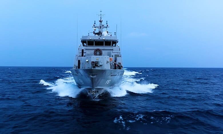 Military ship sailing on the ocean during daytime, with a clear blue sky.