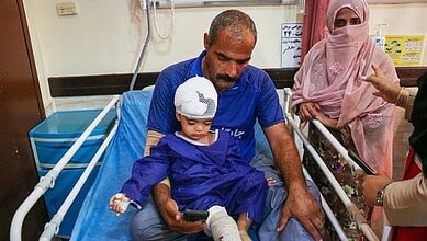 Child in hospital bed with bandaged head, surrounded by family members and medical staff.