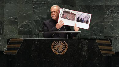 Iran president holding a photo album at UN General Assembly podium.