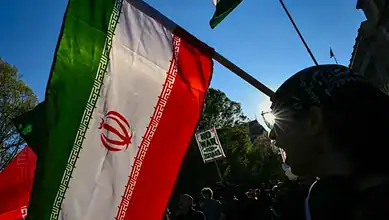 Iran flags being waved at a protest rally during daylight hours.