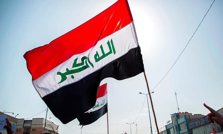 Iraqi flag waving in the sky during daytime with cityscape background.