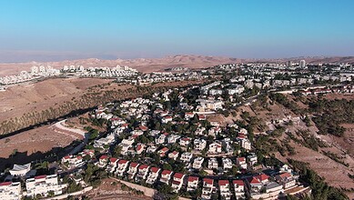 Aerial view of Israeli settlements in the West Bank with surrounding hills and mountains.