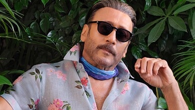 Jackie Shroff wearing sunglasses and floral shirt, posing with greenery background.