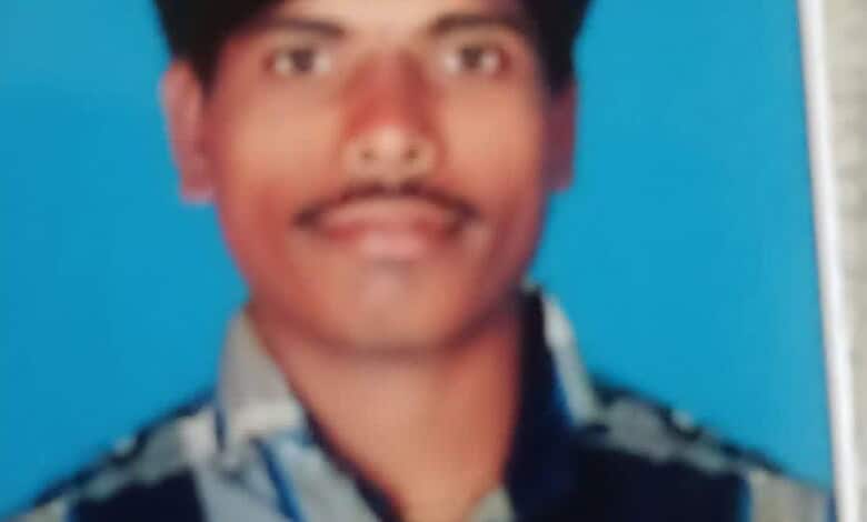 Man with mustache and dark hair, wearing a patterned shirt, against a blue background.