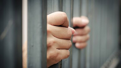 Close-up of a person's hand gripping prison bars, symbolising incarceration.
