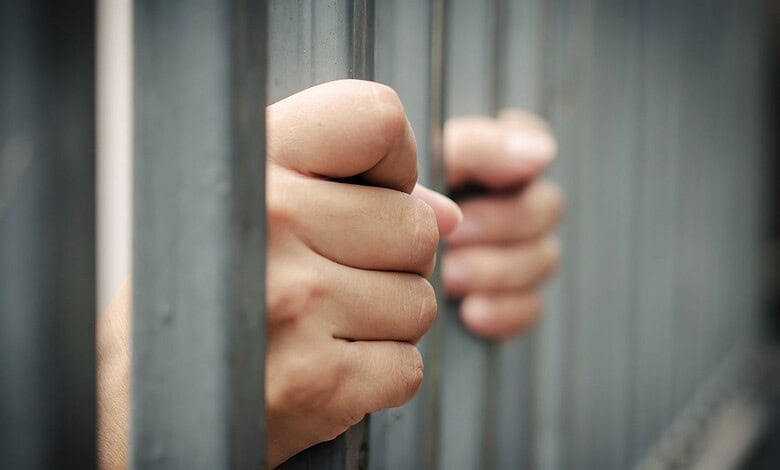 Close-up of a person's hand gripping prison bars, symbolising incarceration.