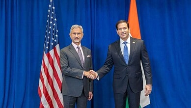 India and US officials shake hands during diplomatic talks at the UN with flags in the background.