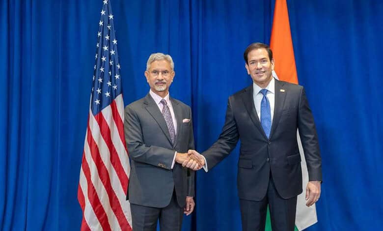 India and US officials shake hands during diplomatic talks at the UN with flags in the background.