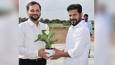 Telangana officials exchange a potted plant during a public event outdoors.
