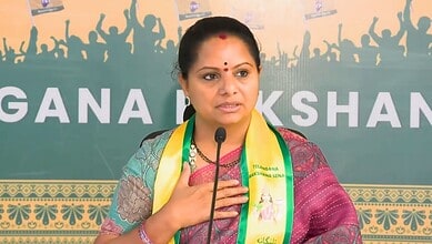 Kavitha speaking at a political event with a backdrop of supporters and banners.
