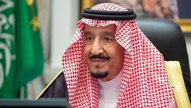 King Salman of Saudi Arabia during an official event, wearing traditional attire and seated at a desk.