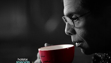 Karan Johar with glasses holding a red coffee mug in black and white image.