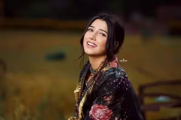 Smiling woman in traditional attire outdoors, vibrant background, natural lighting.
