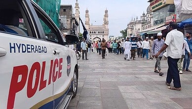 Police vehicle at Makkah Masjid during Friday prayers in Hyderabad with crowds around.