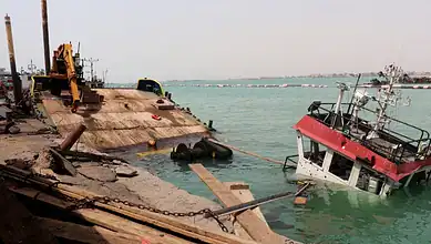 Damaged ship partially submerged near the Yemeni coast with rescue equipment nearby.