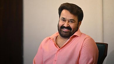 Mohanlal smiling in a pink shirt, seated indoors, promoting the Dubai entertainment event.