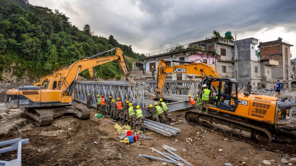 Construction workers and heavy machinery repair flood-damaged infrastructure in Nepal.