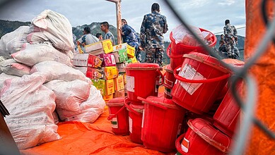 Relief workers prepare supplies including buckets and food packages amid flood response in Nepal.