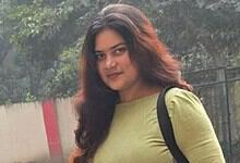 Portrait of a young woman with long dark hair wearing a green top and black backpack.