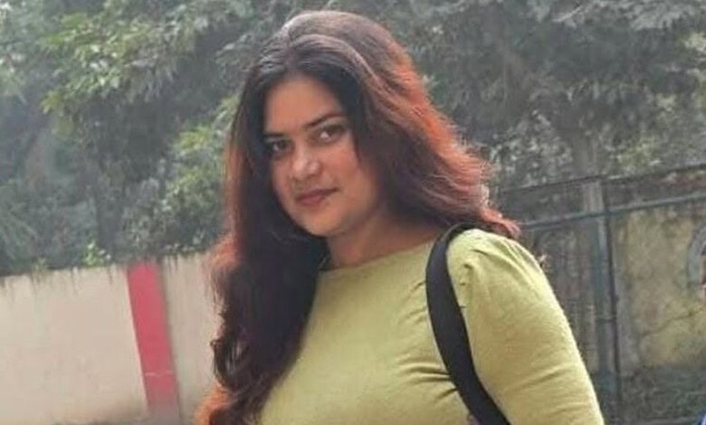 Portrait of a young woman with long dark hair wearing a green top and black backpack.