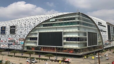 Modern shopping mall with curved glass facade and digital billboards in an urban setting.