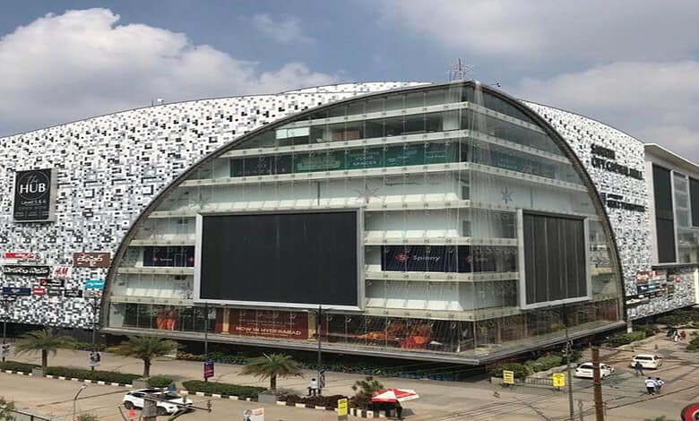 Modern shopping mall with curved glass facade and digital billboards in an urban setting.