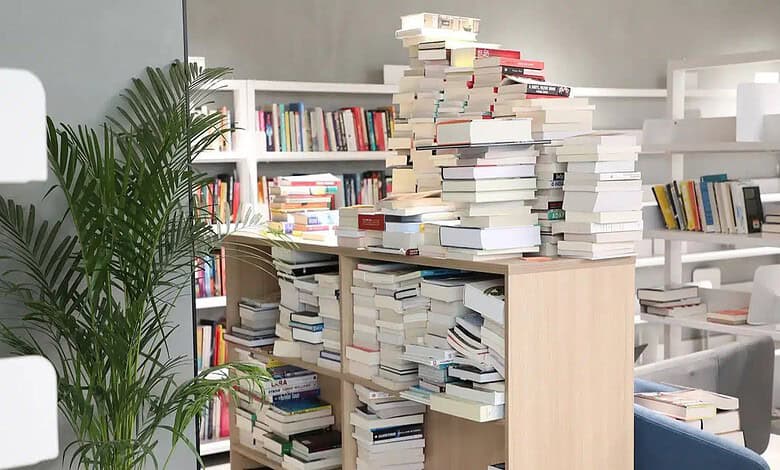 Overflowing bookshelves in a library with a large stack of books on a table.