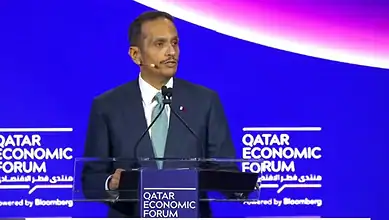Qatar Prime Minister speaking at the Qatar Economic Forum with a blue background and event branding.