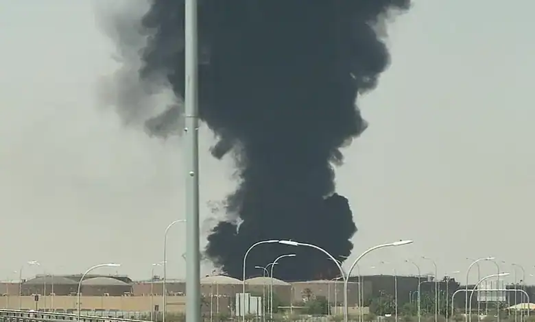 Thick black smoke rising from a fire near Riyadh airport, with clear sky and streetlights in the scene.