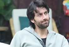 Man with dark hair and beard wearing a light grey hoodie outdoors.