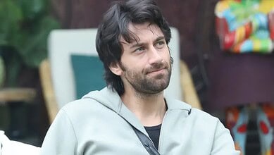 Man with dark hair and beard wearing a light grey hoodie outdoors.