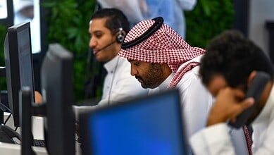 Saudi call center agents providing customer support with headsets and computers.