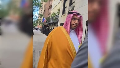 Palestinian American in traditional attire confronts Saudi official outside building.