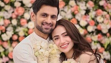 Shoaib Malik and his wife smiling at their wedding celebration with floral backdrop.