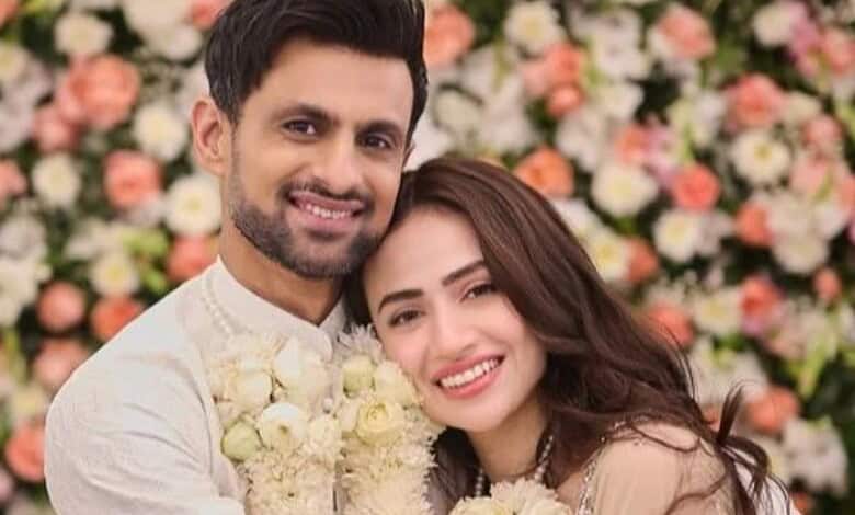 Shoaib Malik and his wife smiling at their wedding celebration with floral backdrop.
