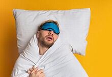Man sleeping with eye mask on pillow against yellow background.