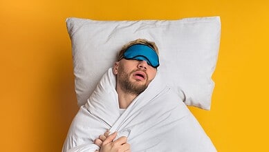 Man sleeping with eye mask on pillow against yellow background.