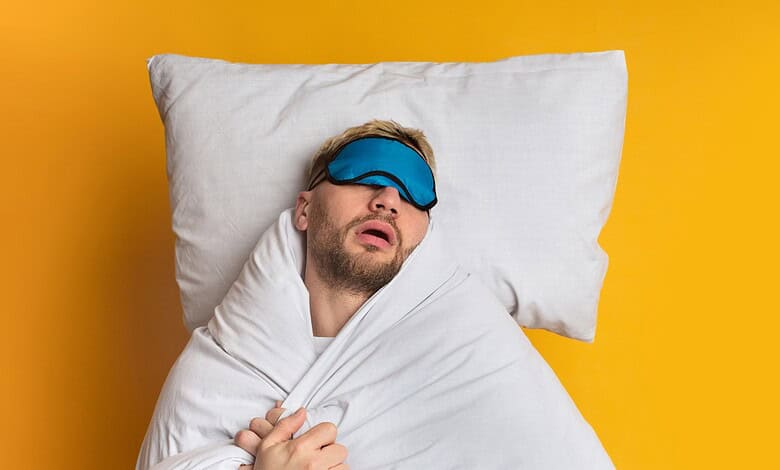 Man sleeping with eye mask on pillow against yellow background.
