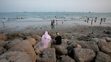 People relaxing on rocks and swimming at the beach during sunset.
