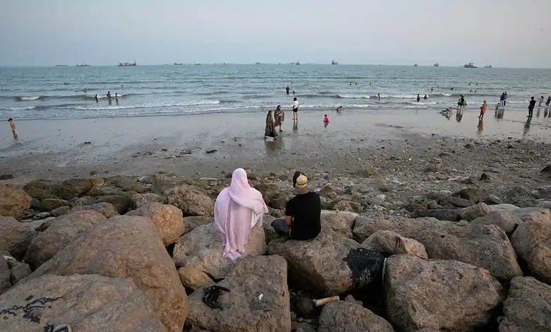 People relaxing on rocks and swimming at the beach during sunset.