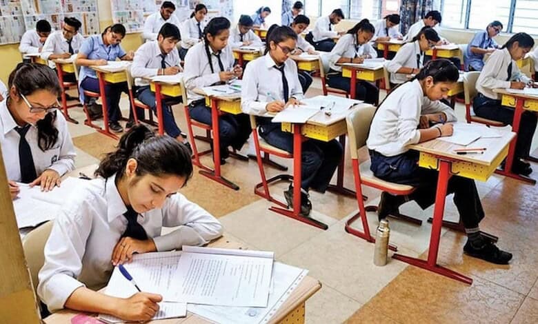 Students in white uniforms taking Class 12 exams in a well-lit classroom.